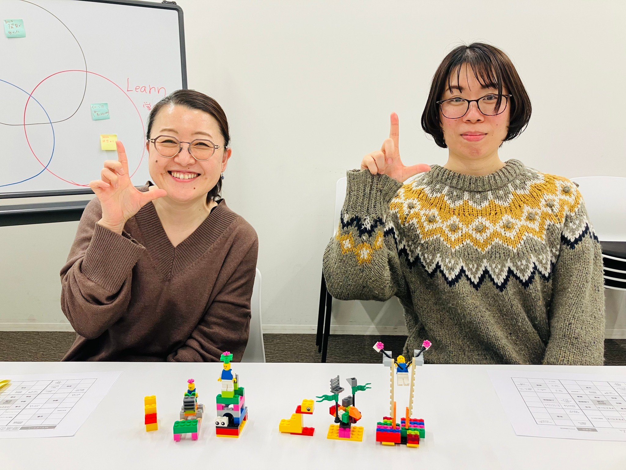 ワークショップ参加者が自作のレゴ®ブロック作品を手に持ち、「L」のポーズで写真撮影。楽しく学びを共有する笑顔のひととき。