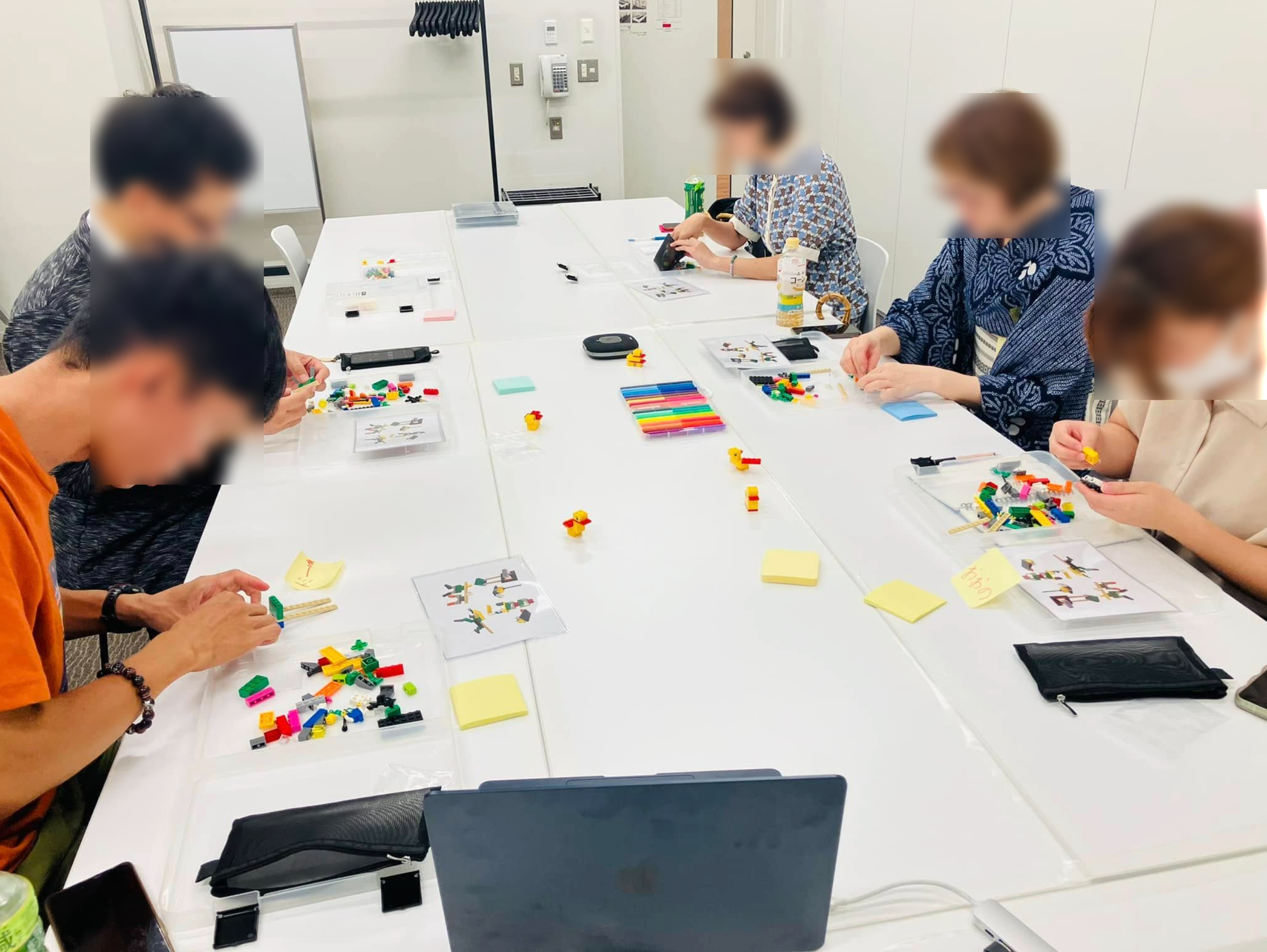 ワークショップ中に参加者がブロックを使って作品を制作している様子。テーブルにはメモや教材が並び、活発に対話が行われている。