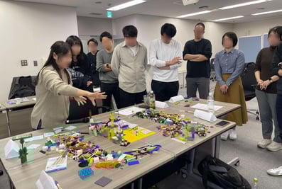 複数のチームがテーブルを囲み、ブロックを使ってディスカッションしている様子。