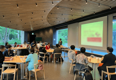 会場内でワークショップが進行する様子。参加者が円卓で意見を交わし、講師が前方で説明を行っている。